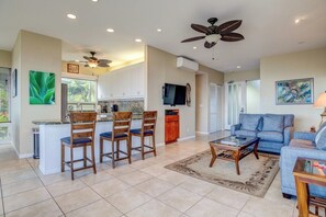 A spacious living area with a blue sofa, a coffee table, and a kitchen with a bar area.