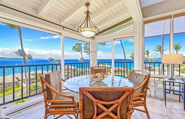 A balcony with a glass table, wicker chairs, and a view of the ocean.
