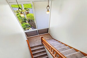 A staircase with carpeted steps and wooden handrails, leading to a room with a window overlooking greenery.