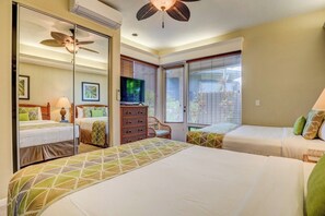 A hotel room with two beds, a television, a ceiling fan, and a large window with blinds.