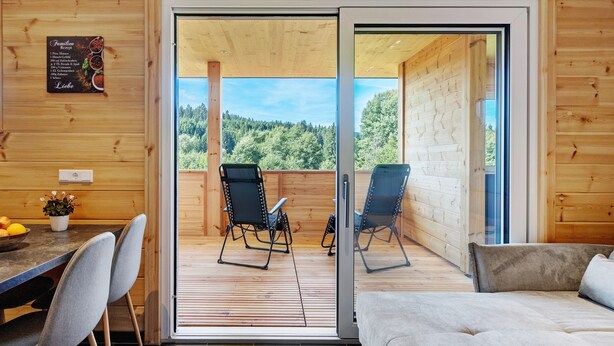 Interior de madera con puerta corredera de vidrio que da a una terraza exterior con sillas y una mesa.