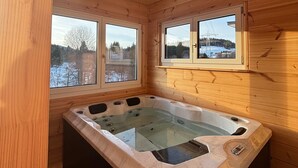 Una cabaña de madera con jacuzzi, ventanas grandes y vistas a un paisaje nevado.