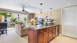 A modern kitchen with a central island, a dining area with a glass balustrade, and a ceiling fan.
