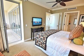A hotel room with a bed, a television, a desk, and a door leading to a balcony.