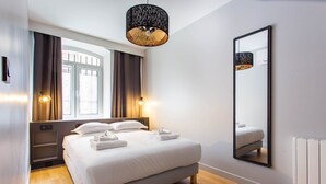 Ein modernes Hotelzimmer mit einem großen Bett, einem Nachttisch, einem Spiegel und einem Fenster mit Vorhängen.