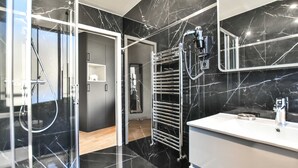 Un baño moderno con suelo de mármol negro, lavamanos blanco y cabina de ducha de vidrio.