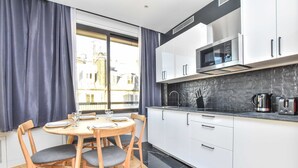Una cocina moderna con armarios blancos, encimera negra y un microondas. Hay una mesa de comedor con sillas y una ventana con cortinas.