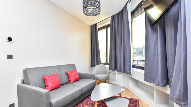 Una sala de estar moderna con un sofá gris, cojines rojos, un sillón gris, una mesita y una alfombra estampada.