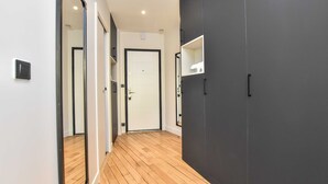 Un pasillo con piso de madera, una puerta blanca y una pared oscura con un estante pequeño y blanco.