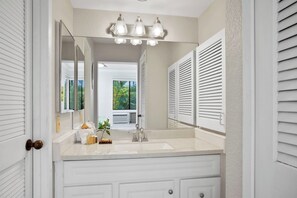 A bathroom with a white vanity, a large mirror, and a window with shutters. - Grand Champions | Ocean View 3 BR, Sleeps 10 | Car Incl. w/ 6+ Nights | GCH ML-1499 by KBM (Wailea)