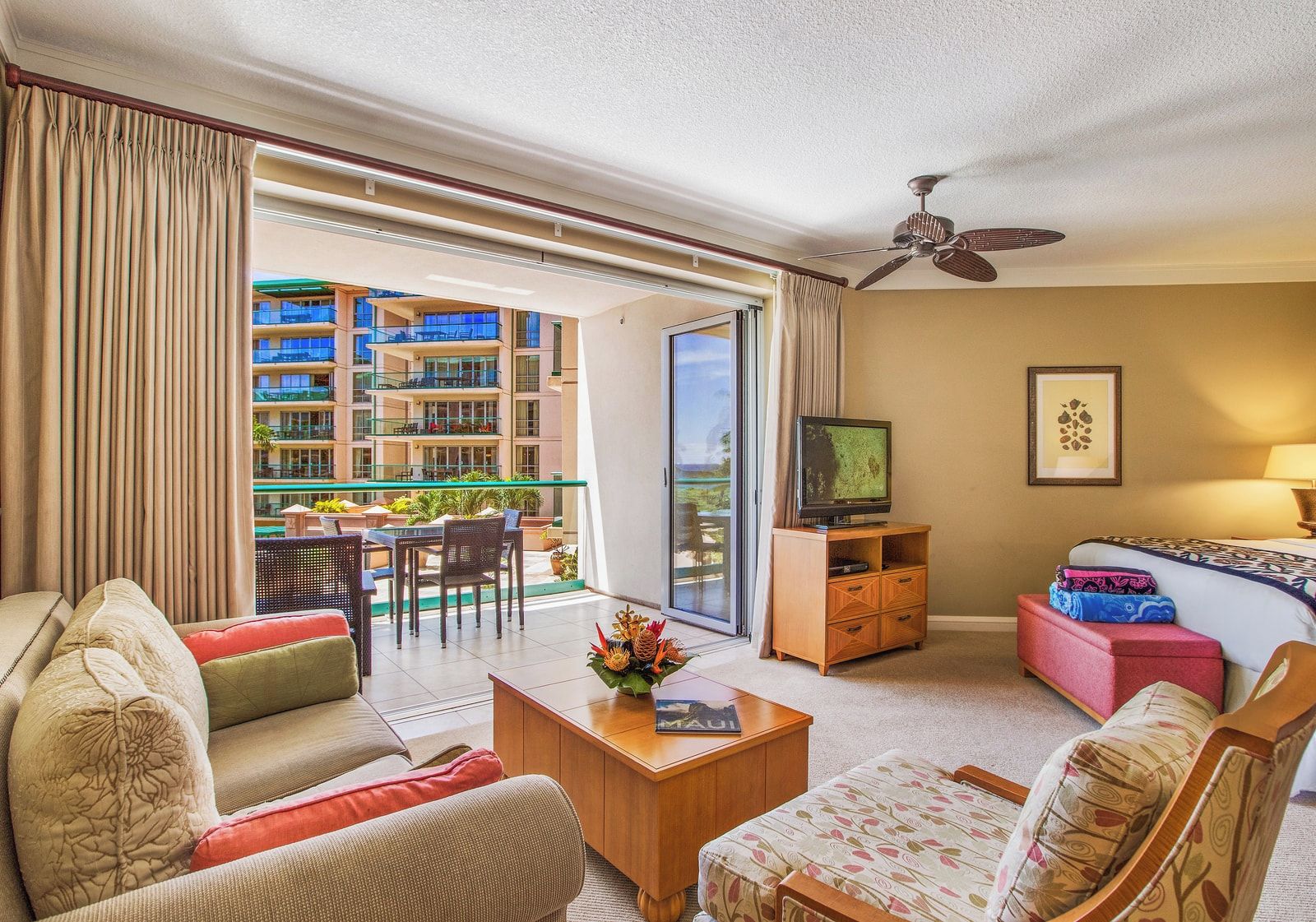 A hotel room with a balcony, a television, a sofa, a coffee table, and a bed.