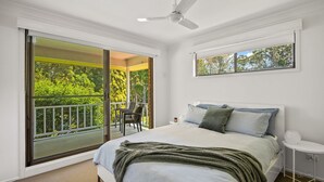 Une chambre avec un lit, un ventilateur de plafond, une fenêtre donnant sur un paysage verdoyant et un balcon avec une chaise.