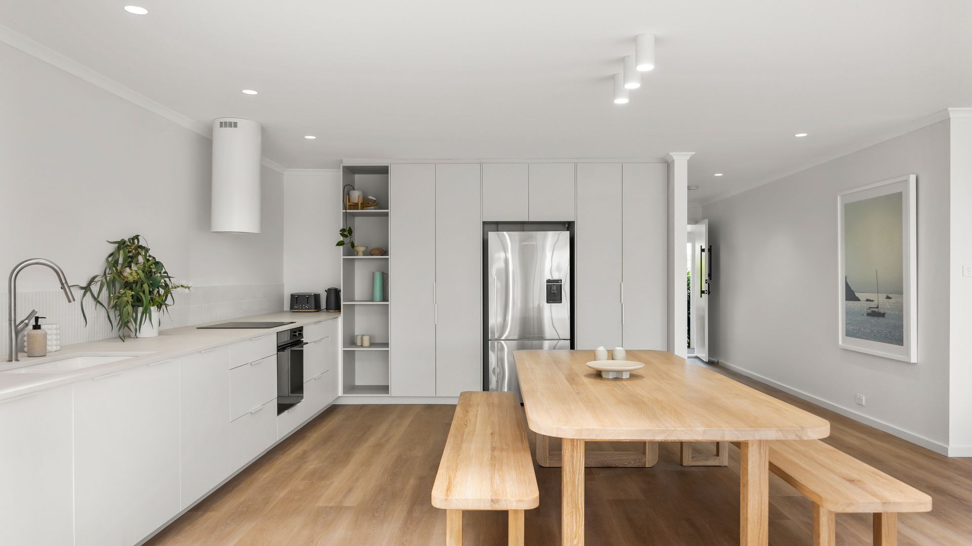 A modern kitchen with white cabinetry, a stainless steel refrigerator, and a wooden dining table with benches.