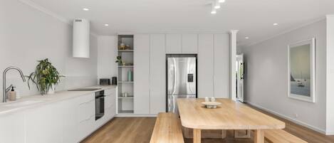 A modern kitchen with white cabinetry, a stainless steel refrigerator, and a wooden dining table with benches.
