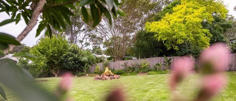 A backyard with a fire pit, a wooden fence, and various trees.