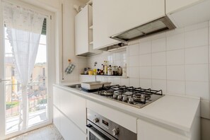 Une cuisine moderne avec des meubles blancs, une cuisinière à gaz et une fenêtre donnant sur des immeubles.