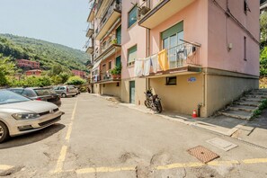 Une rue résidentielle bordée de voitures garées et d’une moto, des immeubles dotés de balcons et, au loin, une colline.