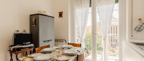 A dining area with a table set for four, a television on a small table, and a view through a glass door.