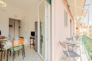 Ein Balkon mit Tisch und Stühlen, eine Tür, die zu einem Zimmer führt, und ein Fernseher im Hintergrund.