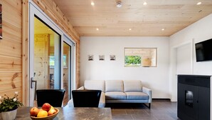 A modern interior with a wooden ceiling, a sofa, a TV, and a kitchen area with a stove. - Mettmapark – Chalet 1 with Private Whirlpool & Sauna, Breakfast Included (Grafenhausen)