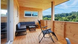 A wooden deck with a sofa, a table, and a chair. - Mettmapark – Chalet 1 with Private Whirlpool & Sauna, Breakfast Included (Grafenhausen)