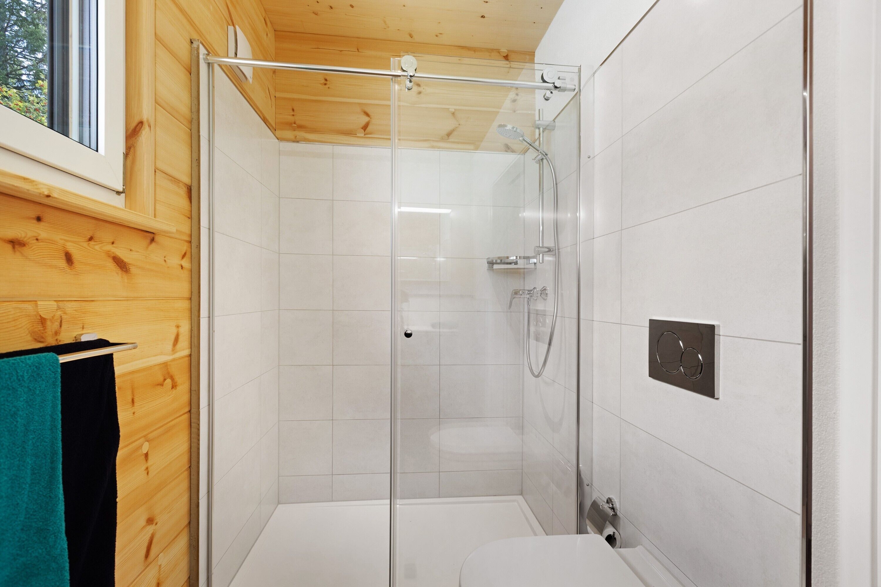 A modern shower with glass doors, a white tiled shower area, and a wooden ceiling.
