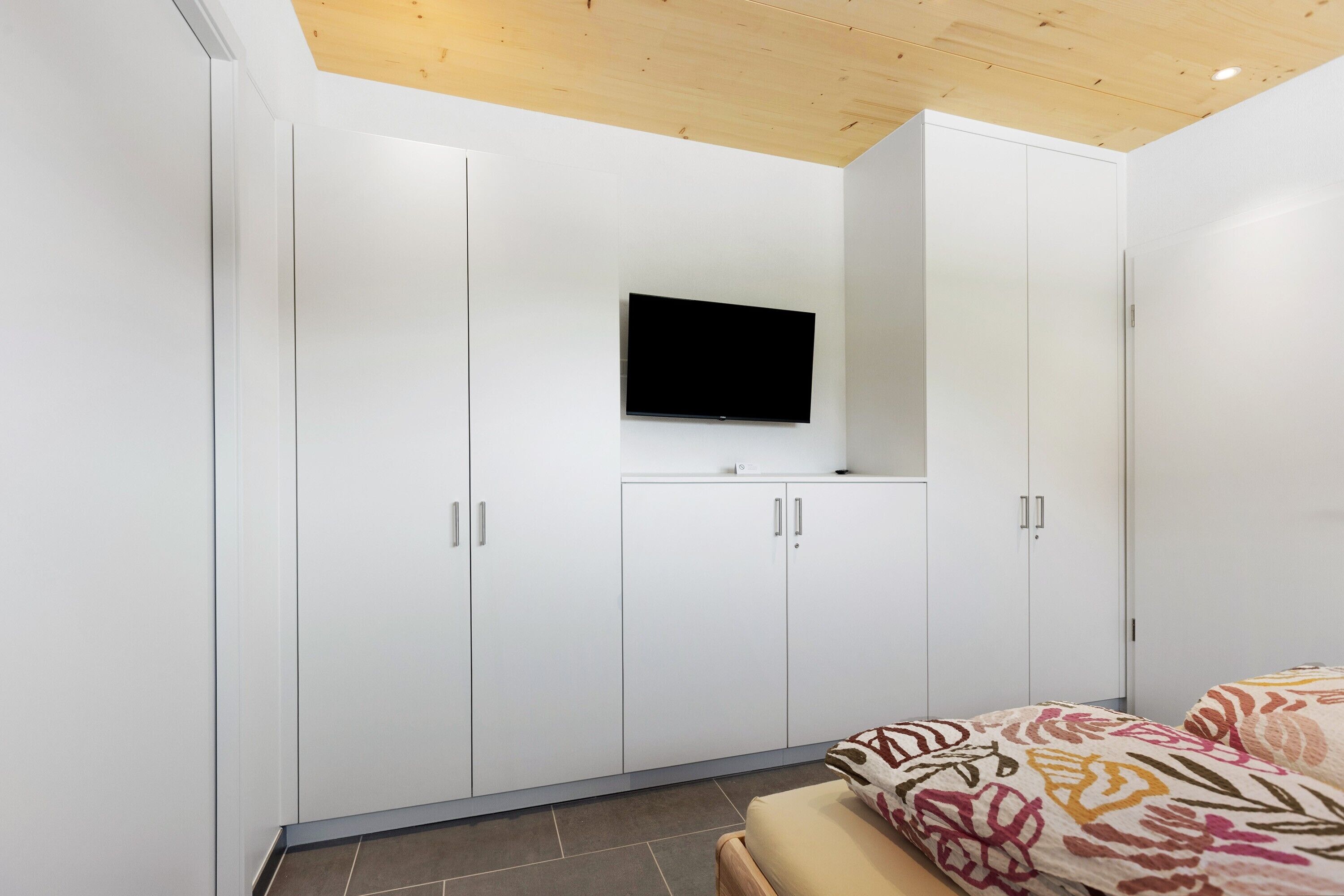 Une chambre à coucher avec un lit, un téléviseur fixé au mur et des armoires blanches.