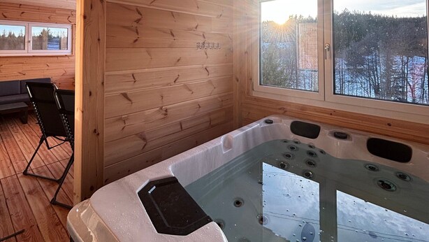 A wooden cabin interior with a hot tub, wooden walls, and a view of a snowy landscape through large windows. - Mettmapark – Chalet 1 with Private Whirlpool & Sauna, Breakfast Included (Grafenhausen)