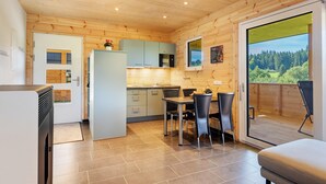 A modern kitchen with wooden walls, a dining area with a table and chairs, and a sliding glass door leading to an outdoor deck. - Mettmapark – Chalet 1 with Private Whirlpool & Sauna, Breakfast Included (Grafenhausen)