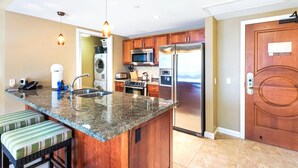 A kitchen with granite countertops, stainless steel appliances, wooden cabinets, and a large island with a sink. - Honua Kai | Ocean View 4 BR, Sleeps 14 | Car Incl. w/ 6+ Nights | HKH ML-1691 by KBM (Lahaina)