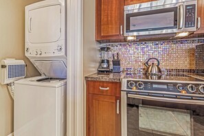 A compact kitchen with a microwave, stove, and washing machine. - Honua Kai | Ocean View 4 BR, Sleeps 14 | Car Incl. w/ 6+ Nights | HKH ML-1694 by KBM (Lahaina)