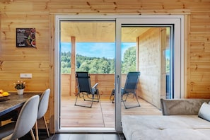 A wooden interior with a sliding glass door leading to an outdoor deck with chairs and a table.