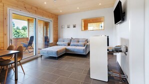 Un interior moderno con un sofá modular, una mesa de comedor, sillas, un televisor de pantalla plana y un calentador de agua a la vista.