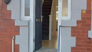 Une porte d’entrée avec un vantail sombre et un cadre de couleur claire, qui donne sur un escalier.