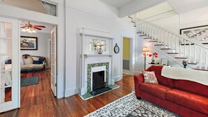 A spacious living room with a fireplace, a red sofa, and a staircase. - Historic Charm in Grand Gulfport Home; walk to beach, casino, port, aquarium (Gulfport)