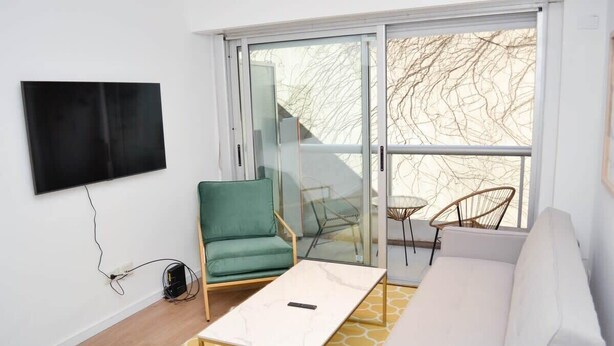 A modern living room with a large window, a flat-screen TV mounted on the wall, a green armchair, a white sofa, and a small table. - Buenos Aires: Palermo. Perfect for digital nomads. (Buenos Aires)