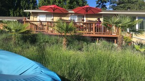 A wooden deck with red umbrellas, surrounded by tall trees and a blue sky.