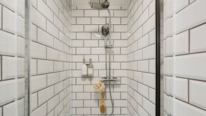 Une douche aux carreaux blancs, une douchette à main et une brosse à main.
