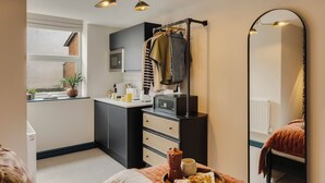 Une cuisine de taille réduite, dotée d’une fenêtre, d’un plan de travail noir et d’une étagère suspendue où sont accrochés des vêtements.
