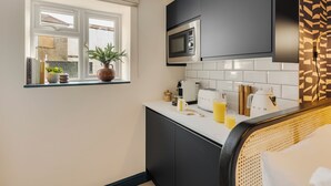 Een moderne keuken met een magnetron, broodrooster en waterkoker op het aanrecht. Er is een raam met planten op de vensterbank en een witte betegelde spatwand.