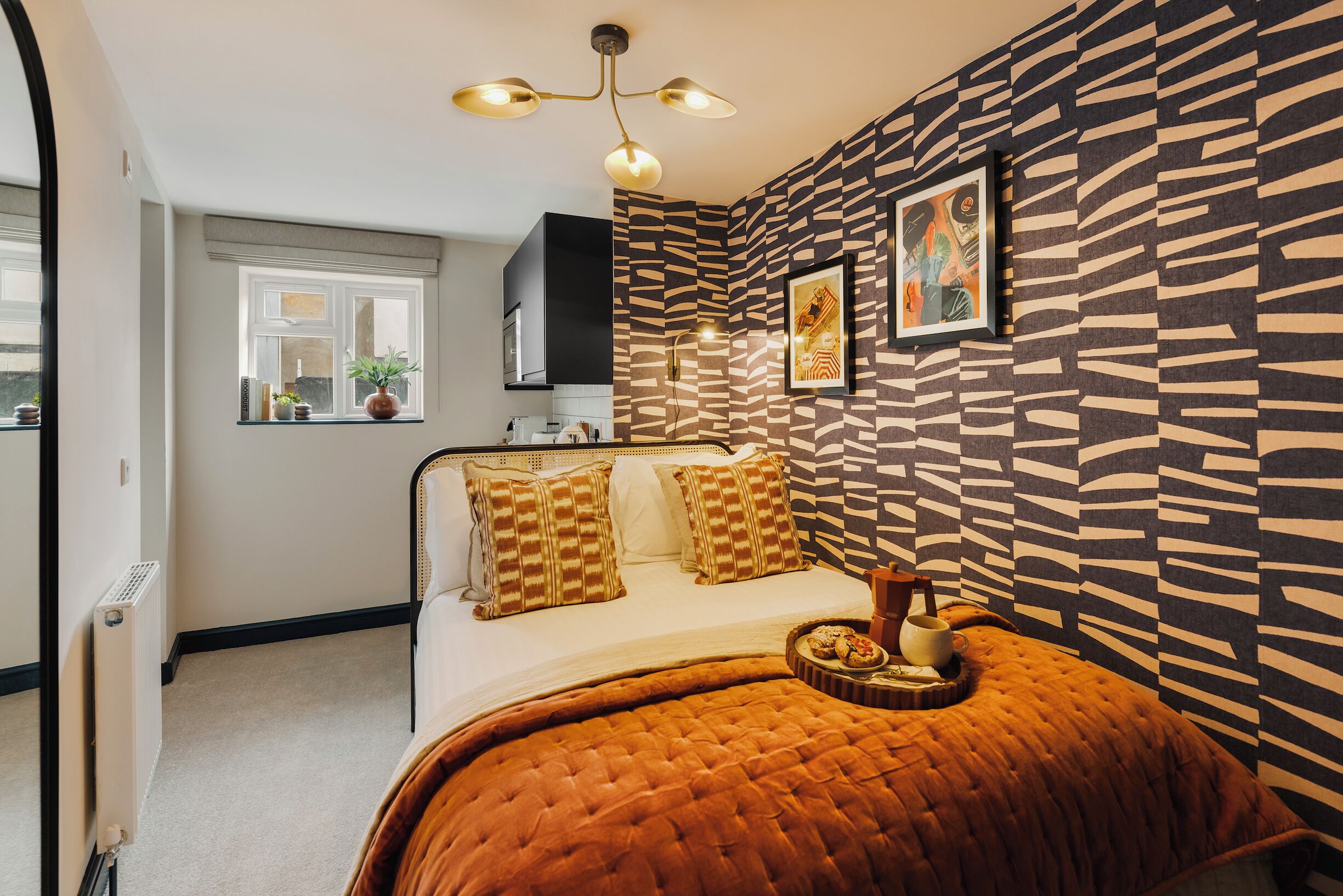 A bedroom with a bed, a window, a radiator, and a patterned wall.