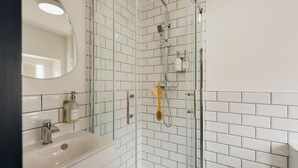 Een moderne badkamer met een douchecabine van glas, een wit wastafeltje en een spiegel.