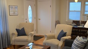 Ein Wohnzimmer mit Deckenventilator, zwei Sesseln, einem Sofa, einem Couchtisch und einem Essbereich mit Tisch und Stühlen.