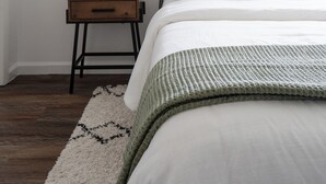 A neatly arranged bedroom with a bed, bedside table, lamp, and a potted plant.