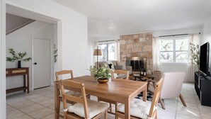 A dining area with a wooden table and chairs, a stone fireplace, and a television on a black cabinet.