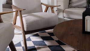 A modern living room with a light-colored armchair, a wooden coffee table, and a patterned rug.