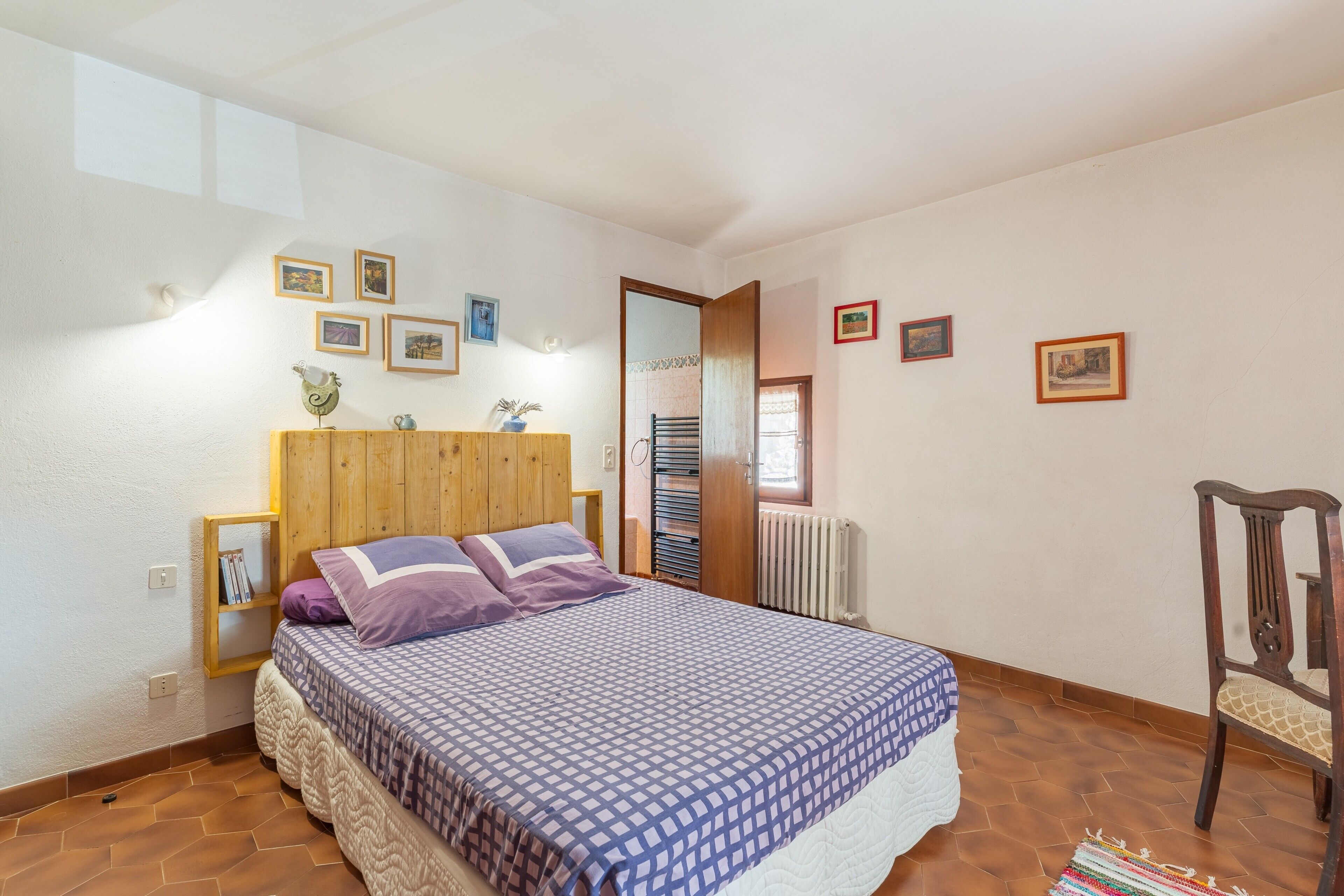 A bedroom with a bed, a wooden headboard, a radiator, a chair, and framed pictures on the wall.