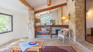 A cozy room with exposed wooden beams, a stone wall bookshelf, a wicker chair, and a view through a window. - Holiday Home 'Bastide Provençale' with Private Pool, Private Terrace and Private Garden (Caseneuve)