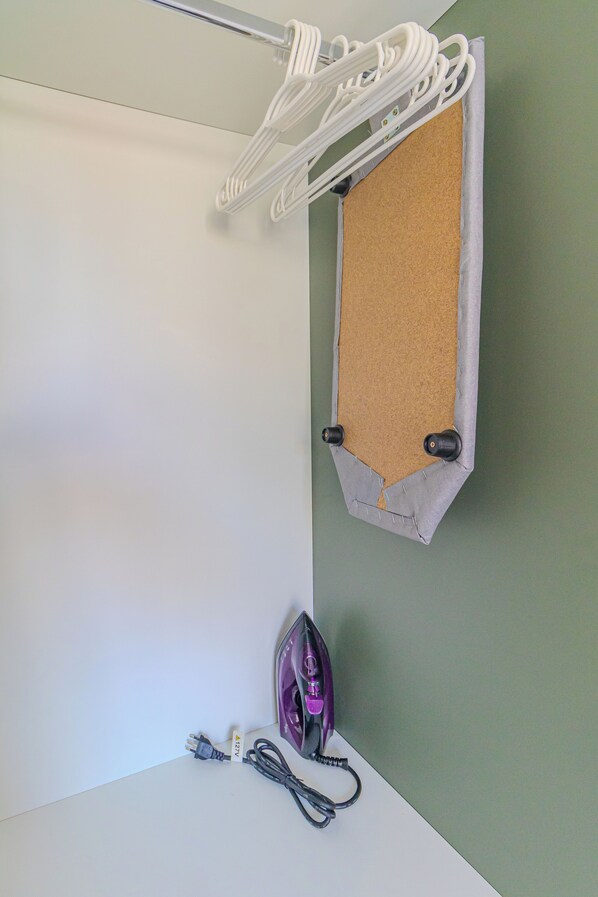 A wall-mounted corkboard with a white hanging rack above it, an iron, and a power cord on the floor. - Urbic Sabiá (São Paulo)