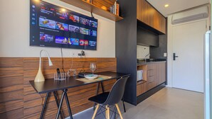 A modern kitchen with a flat-screen TV mounted above a wooden dining table, a wine glass, and a bowl. - Urbic Sabiá (São Paulo)